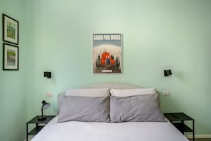 A bedroom with a bed, two bedside tables, a wall-mounted poster, and two wall-mounted lamps. - New Flat with Artistic Flair (Milano)