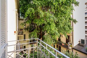 A multi-story building with balconies, a staircase, and a large tree providing shade. - New Flat with Artistic Flair (Milano)