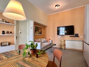 A modern living room with a dining table, chairs, a sofa, a television, and a radiator. - New Flat with Artistic Flair (Milano)