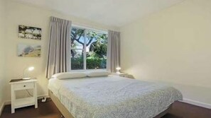 Une chambre à coucher avec un lit, des tables de chevet, une fenêtre avec des rideaux et une petite table de nuit.