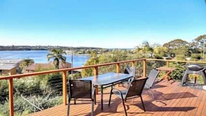 Eine Terrasse mit Tisch und Stühlen, mit Blick auf ein Gewässer und viel Grün.