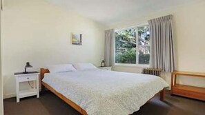 Ein Schlafzimmer mit einem Bett, einem Nachttisch, einem Fenster mit Vorhängen und einer Heizung.