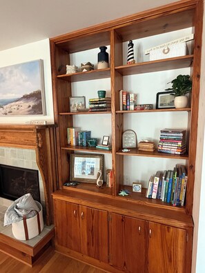 Ein Holzregal mit verschiedenen Büchern, Dekoration und einem gerahmten Bild von einer Strandlandschaft.