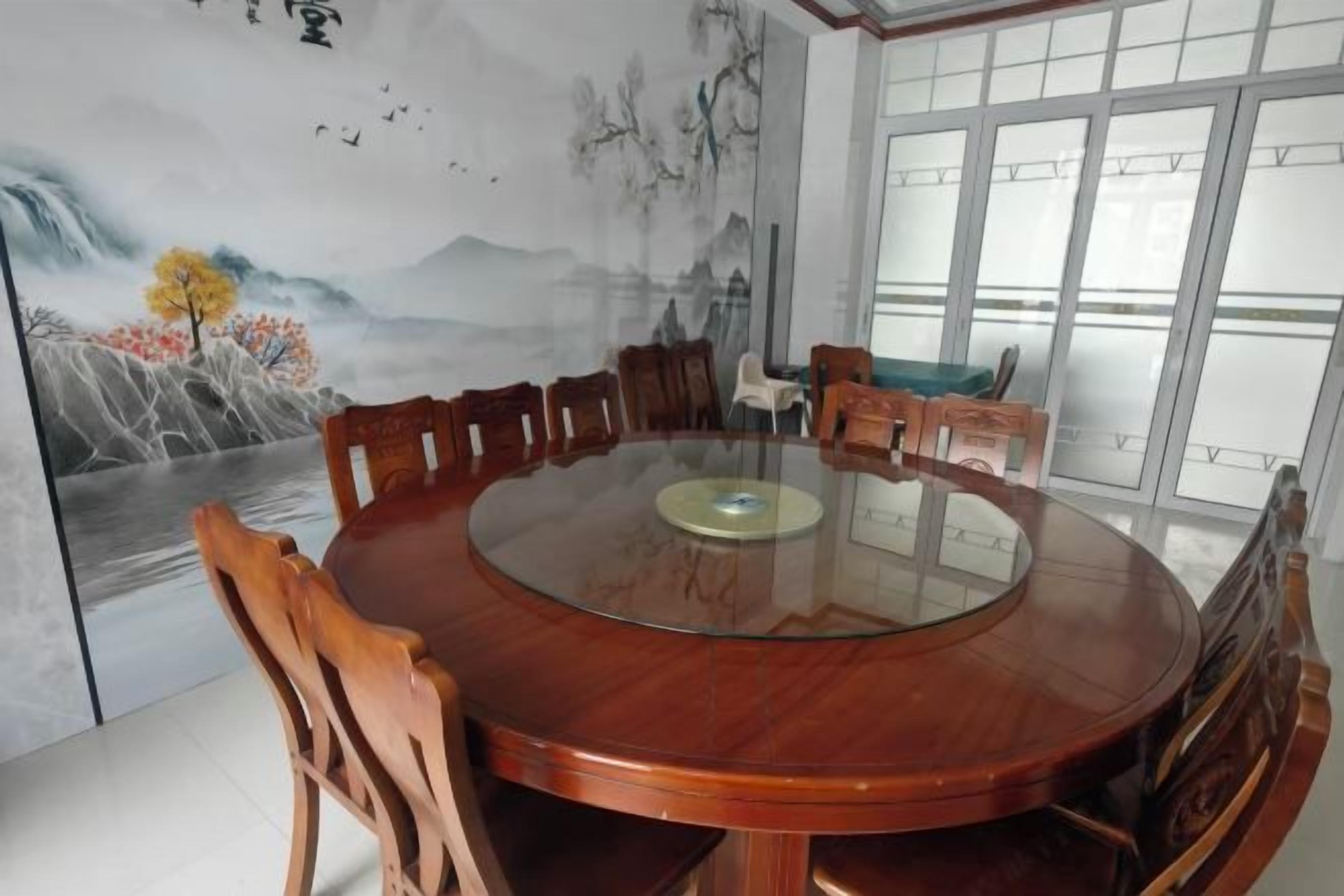 Ein runder Holzesstisch mit Stühlen, einer Glasplatte und einem Wandgemälde.