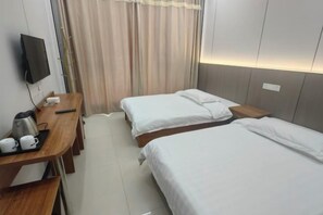 A hotel room with two beds, a desk with a coffee maker, a television, and a curtain.