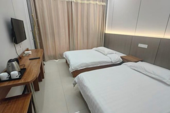 A hotel room with two beds, a desk with a coffee maker, a television, and a curtain.