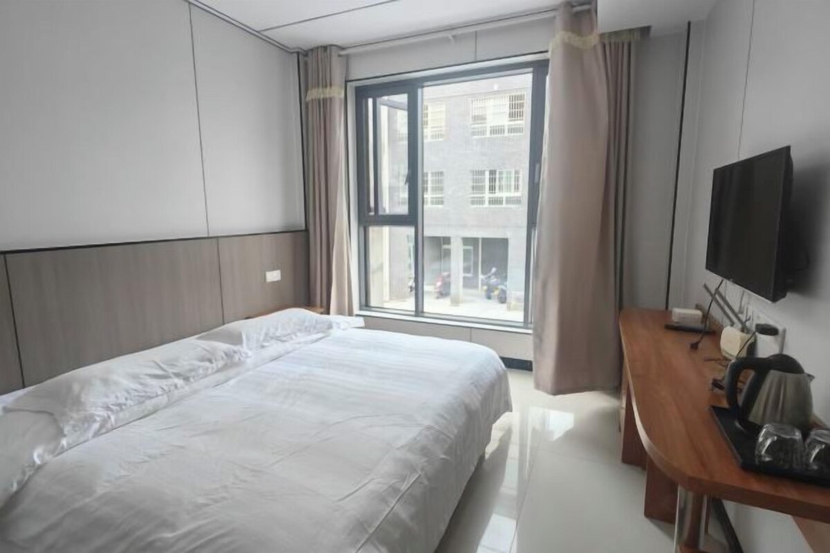 A hotel room with a bed, a desk, a television, and a window with curtains.