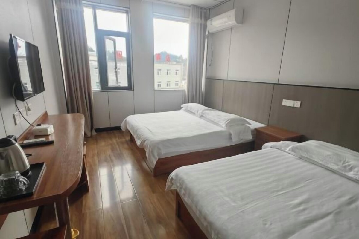 A hotel room with two beds, a desk with a kettle, and a television.