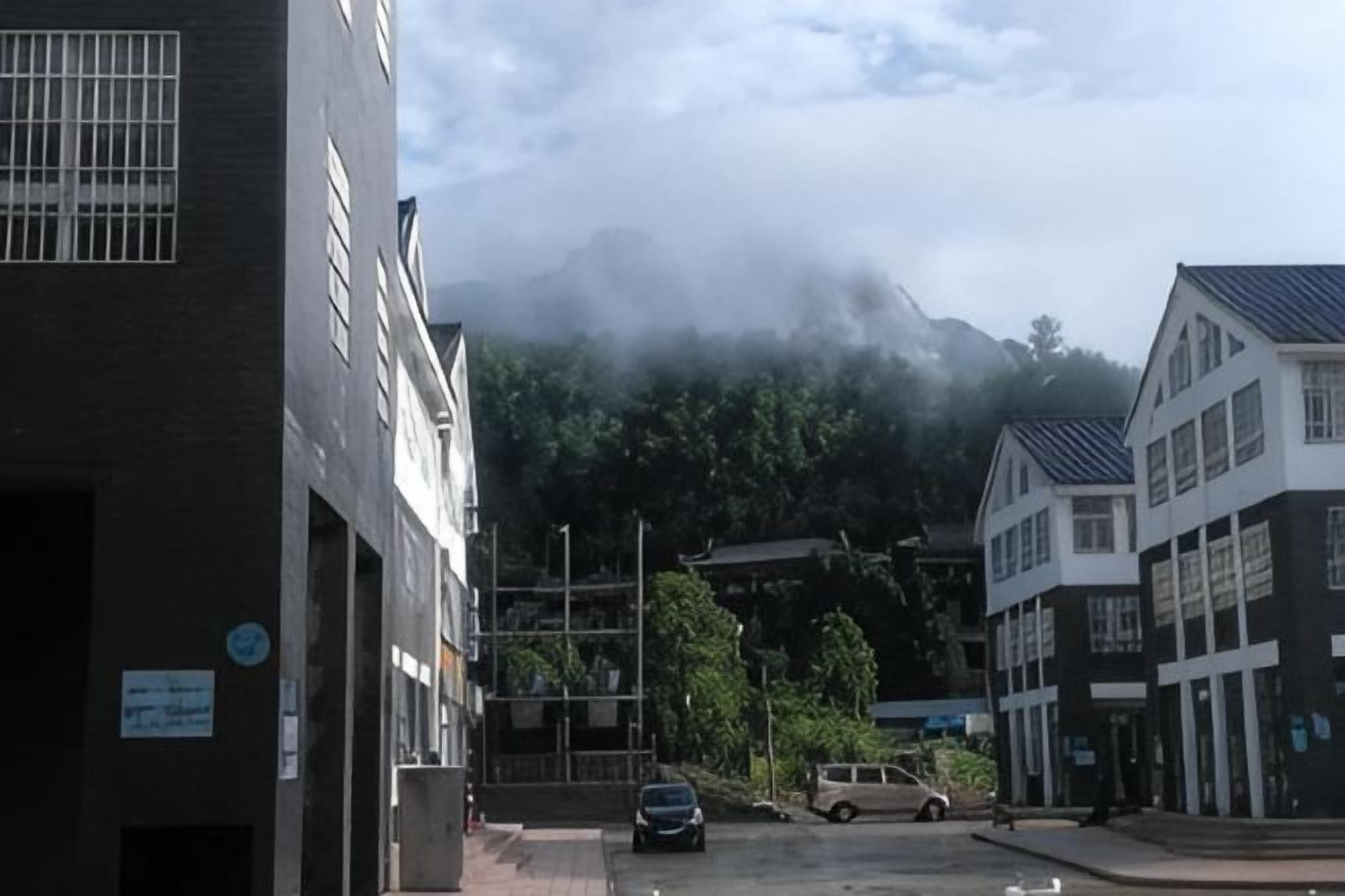 A street with buildings, a parked car, and a mountain in the background.