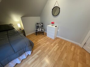 A bedroom with a bed, a chair, a dresser, and a mirror on the wall.