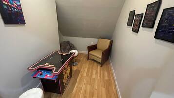 A small room with a pinball machine, a white chair, and framed pictures on the wall.