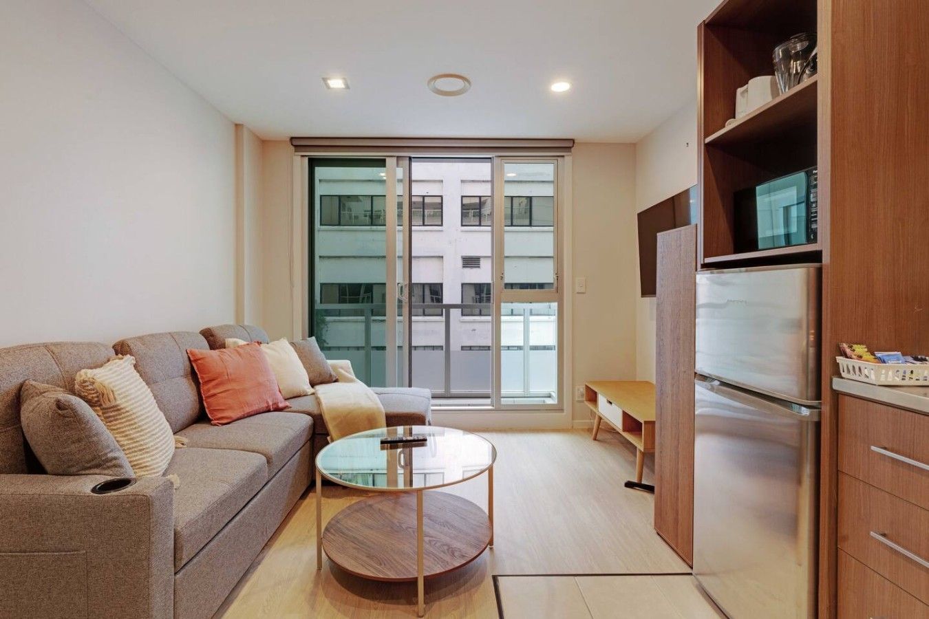 Una sala de estar moderna con un sofá, una mesa de centro de vidrio, un mueble de madera y un ventanal corredero al exterior.