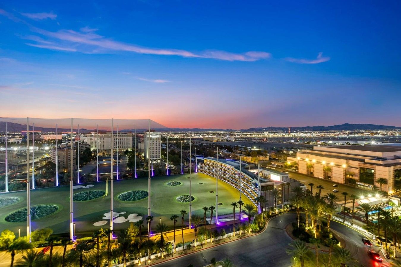 A large hotel complex with multiple buildings, a central courtyard with palm trees, and a view of the cityscape at dusk.