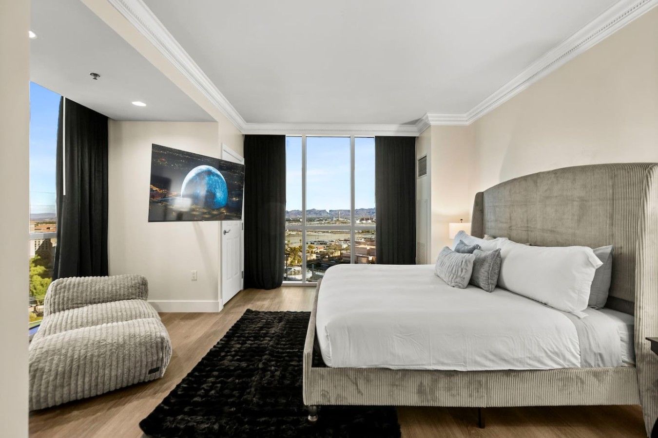 A bedroom with a large bed, a sofa, a TV, and a view of a cityscape.