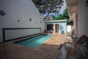 Piscina com bordas azulejadas, mesa de vidro e cadeiras de vime.