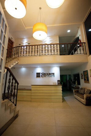 Vestíbulo de hotel con mostrador de recepción, una escalera y un área de estar.