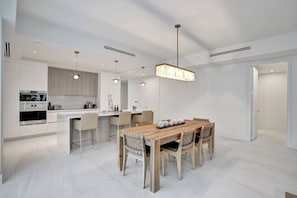 A modern kitchen with a dining area, featuring a central island, pendant lighting, and a built-in oven. - Oceanview 3BR Steps to Sand & Pool, Pompano (Pompano Beach)