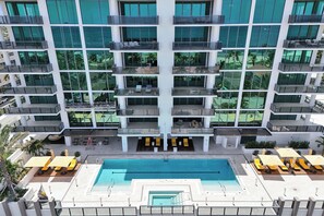 Ein mehrstöckiges Hotel mit einem zentralen Schwimmbecken, Sitzgelegenheiten im Freien und Balkonen.
