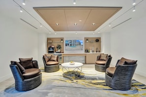 Ein moderner Lounge-Bereich mit einem runden Tisch in der Mitte, Sitzgelegenheiten mit Kissen und einem großen Gemälde an der Wand.