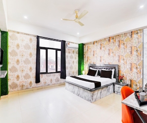 A hotel room with a bed, a desk, a chair, a ceiling fan, and a window with a view. - Classic Grand Jvi Resort & Marriage Lawn (Faizabad)
