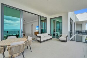 A modern outdoor living space with a dining area, seating, and a view of the ocean. - Oceanfront 3BR | Balcony, Pool & Beach Steps (Pompano Beach)
