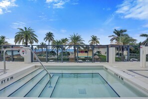 A swimming pool with clear water, surrounded by palm trees and a clear sky. - Oceanfront 3BR | Balcony, Pool & Beach Steps (Pompano Beach)