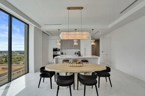 A modern kitchen with a central island, pendant lighting, and a dining area with a round table and chairs. - Oceanfront 3BR | Balcony, Pool & Beach Steps (Pompano Beach)