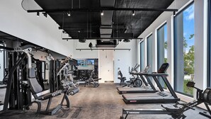 Et fitnesscenter med forskellig træningsudstyr, herunder løbebånd og styrkemaskiner, store vinduer og udsigt til det fri.