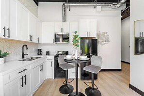A modern kitchen with white cabinets, a black refrigerator, a stove, and a dining area with a round table and two chairs. - Downtown Nights Await Petco Park & Gaslamp Fun!! (San Diego)
