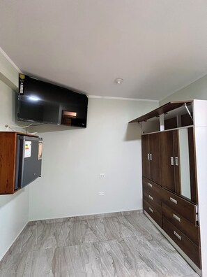 A room with a flat-screen TV mounted on the wall, a built-in wardrobe with multiple drawers, and a tiled floor.