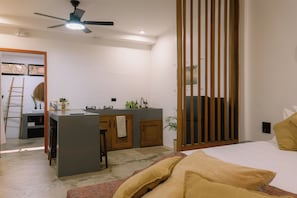 A modern bedroom with a bed, a desk with a chair, a small kitchen area, and a sliding door.