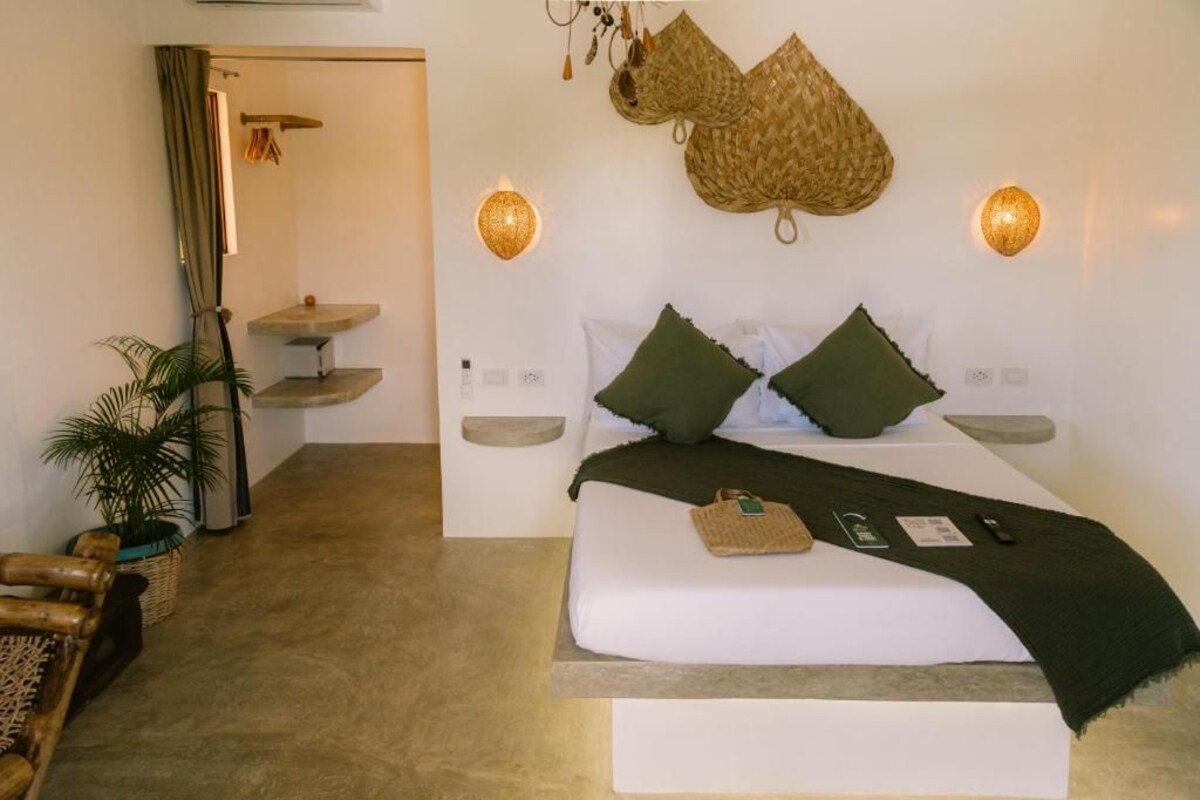 Un dormitorio con cama, mesitas de noche, una cesta colgante y una pequeña mesa con una planta.