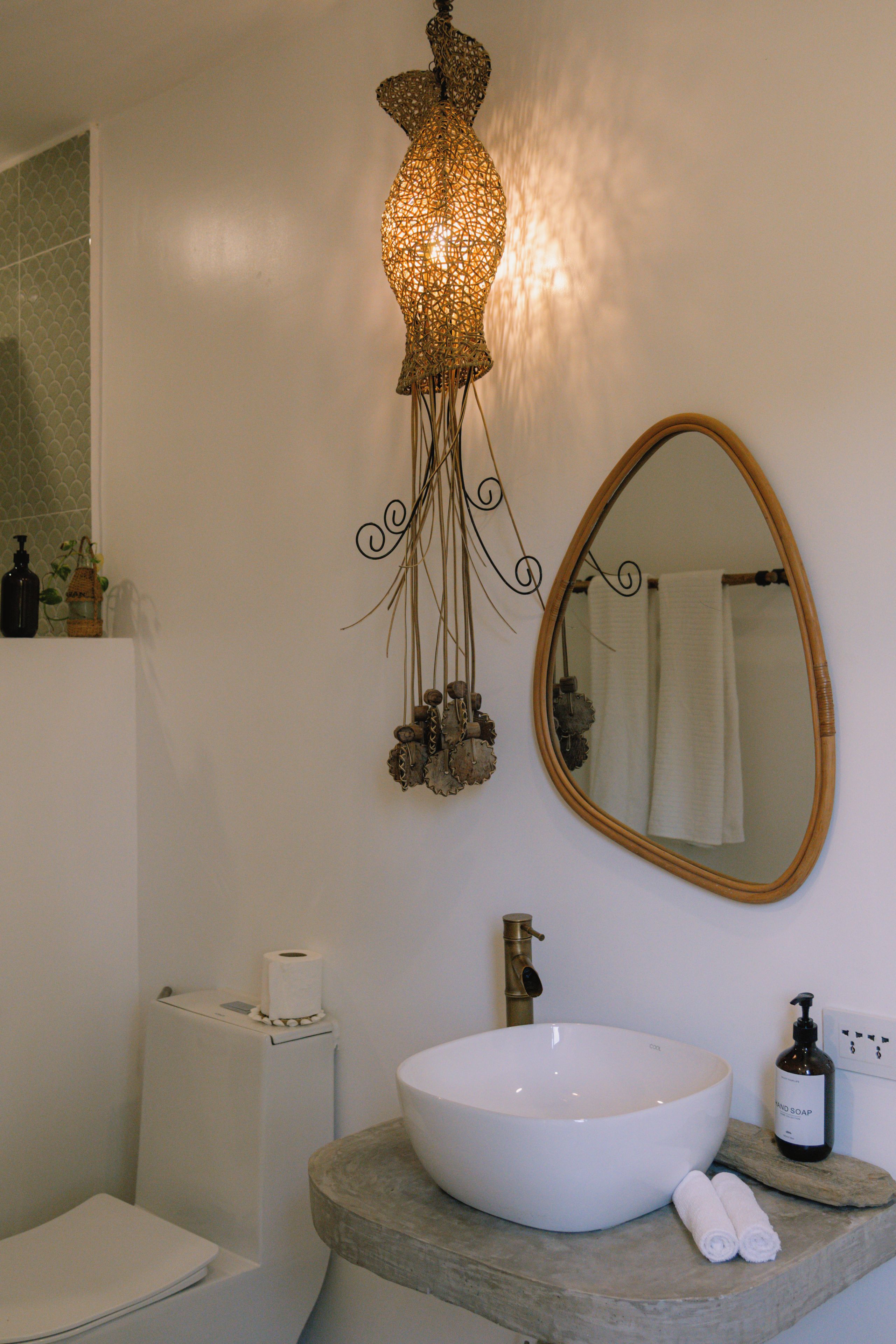 Een badkamer met een wit wastafel, een spiegel, een hanglamp en een toilet.