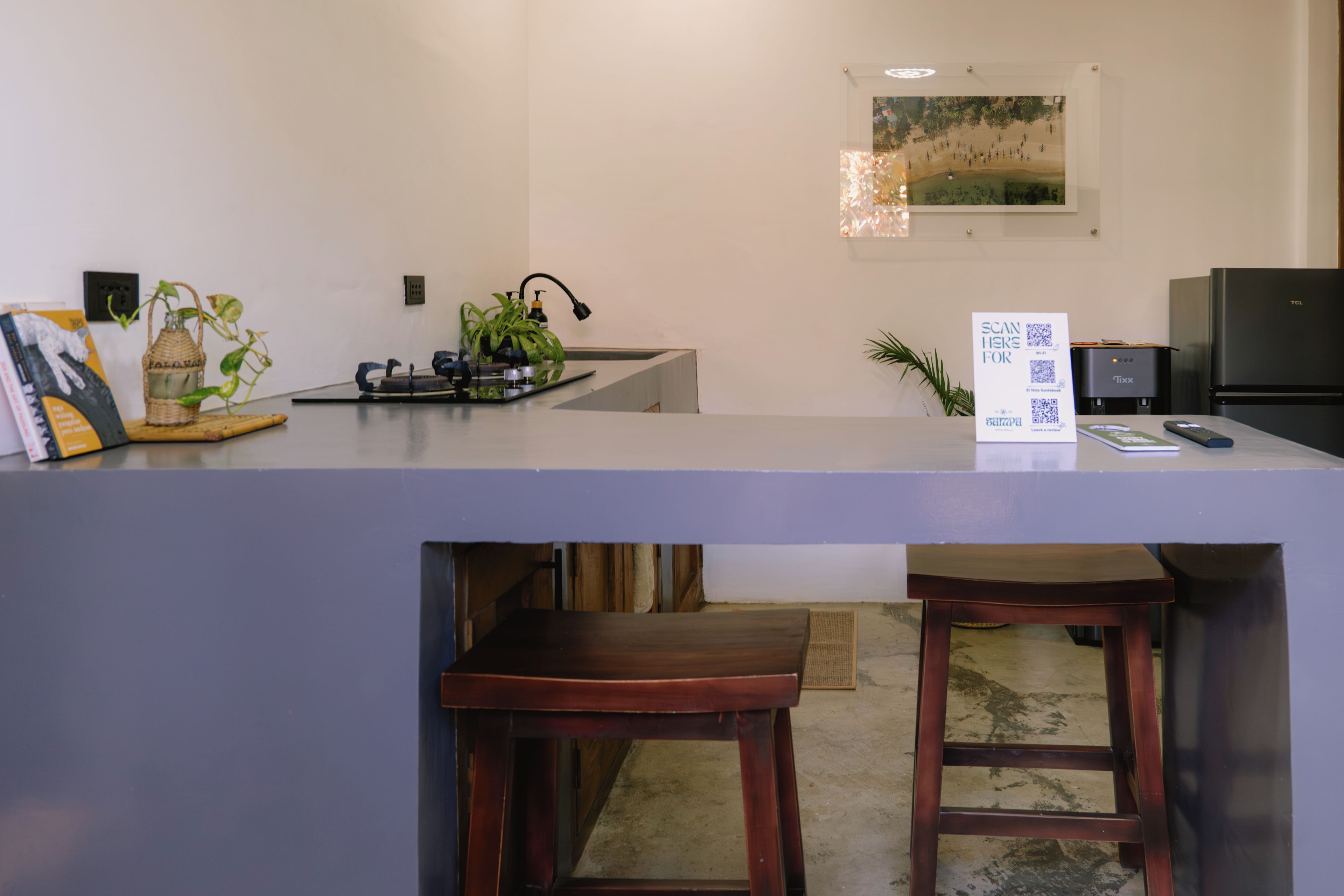 Une cuisine équipée d’un comptoir, de tabourets, d’un réfrigérateur, d’un évier et d’un tableau accroché au mur.
