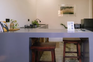 A kitchen with a counter, stools, a refrigerator, a sink, and a wall-mounted picture.