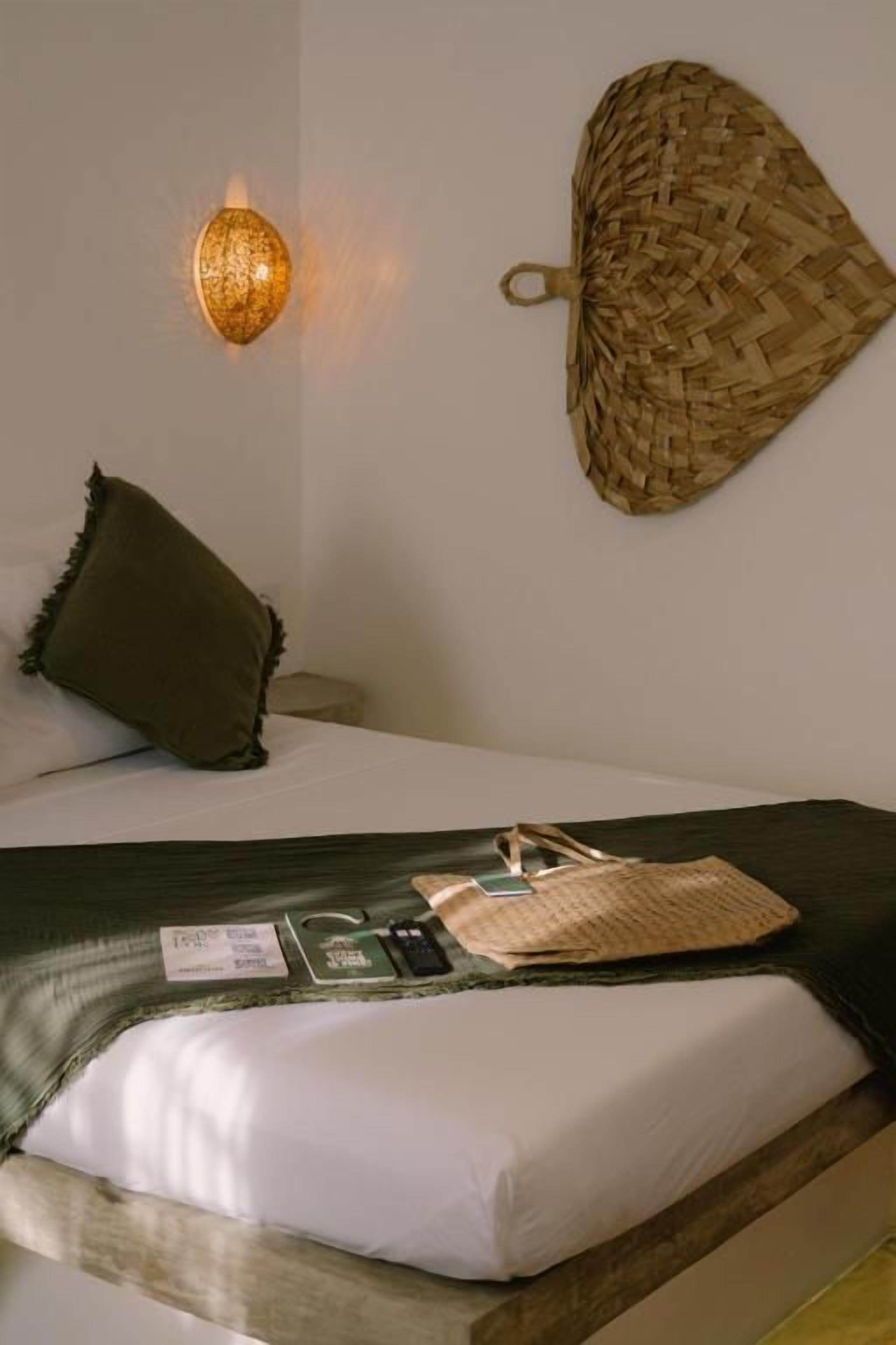 Een bed met een groene deken, een geweven mand en een wandlamp.