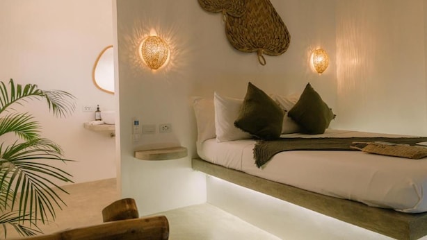 A bedroom with a bed, pillows, a bedside table, a wall-mounted lamp, and a hanging woven basket. - SAMPA El Nido (El Nido)