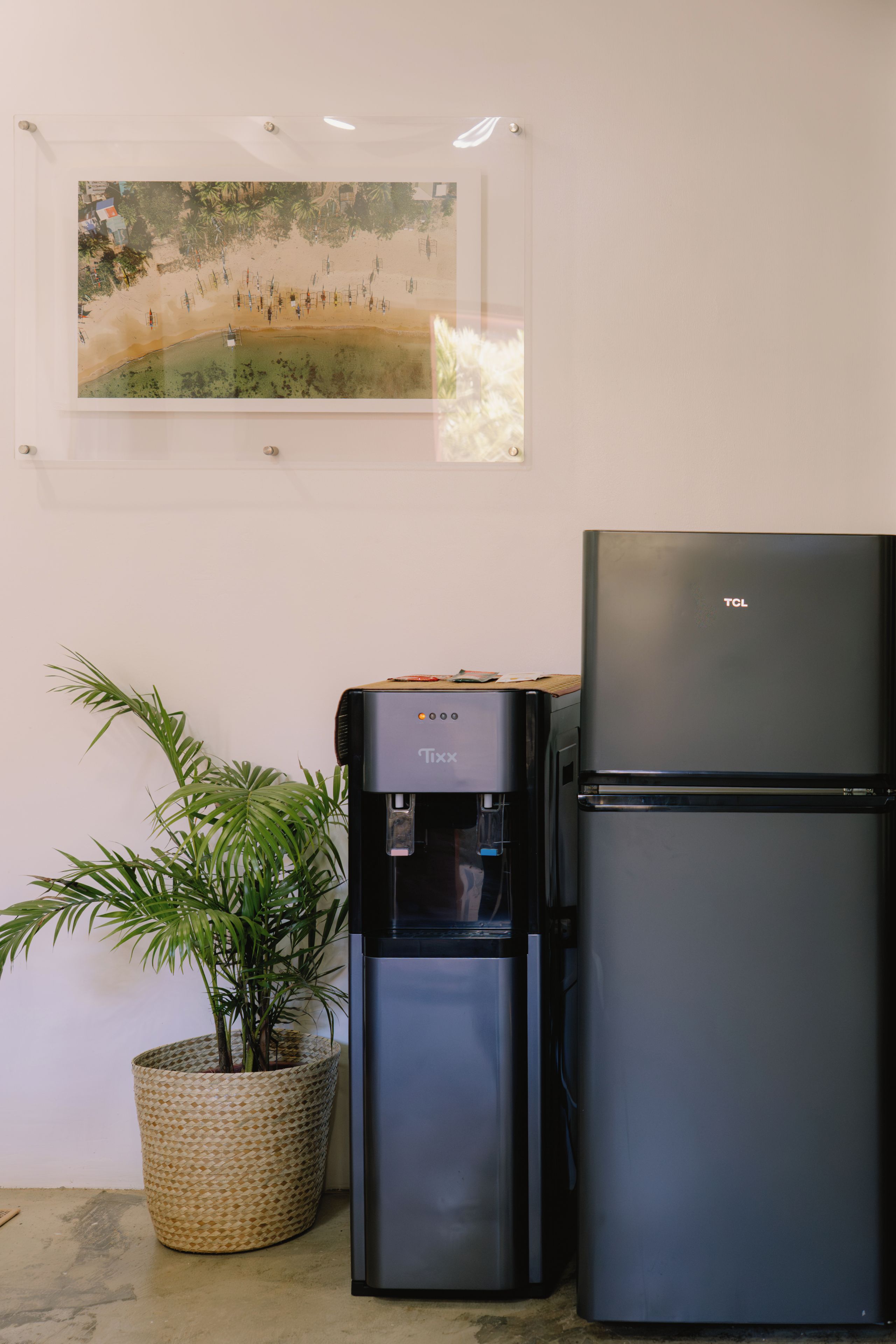 A water dispenser and a refrigerator in a room with a framed picture on the wall.