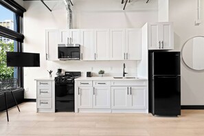 A modern kitchen with white cabinets, a black stove, a black refrigerator, and a window with a view of buildings. - Petco Park Nearby Walk to Gaslamp, Dine & Explore (San Diego)