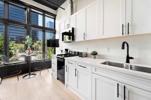 A modern kitchen with white cabinets, a black stove, and a large window overlooking a cityscape. - Petco Park Nearby Walk to Gaslamp, Dine & Explore (San Diego)