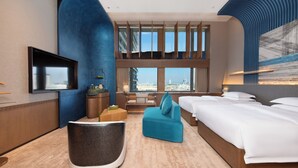 Een hotelkamer met een groot bed, een bank, een televisie en uitzicht op de stad.