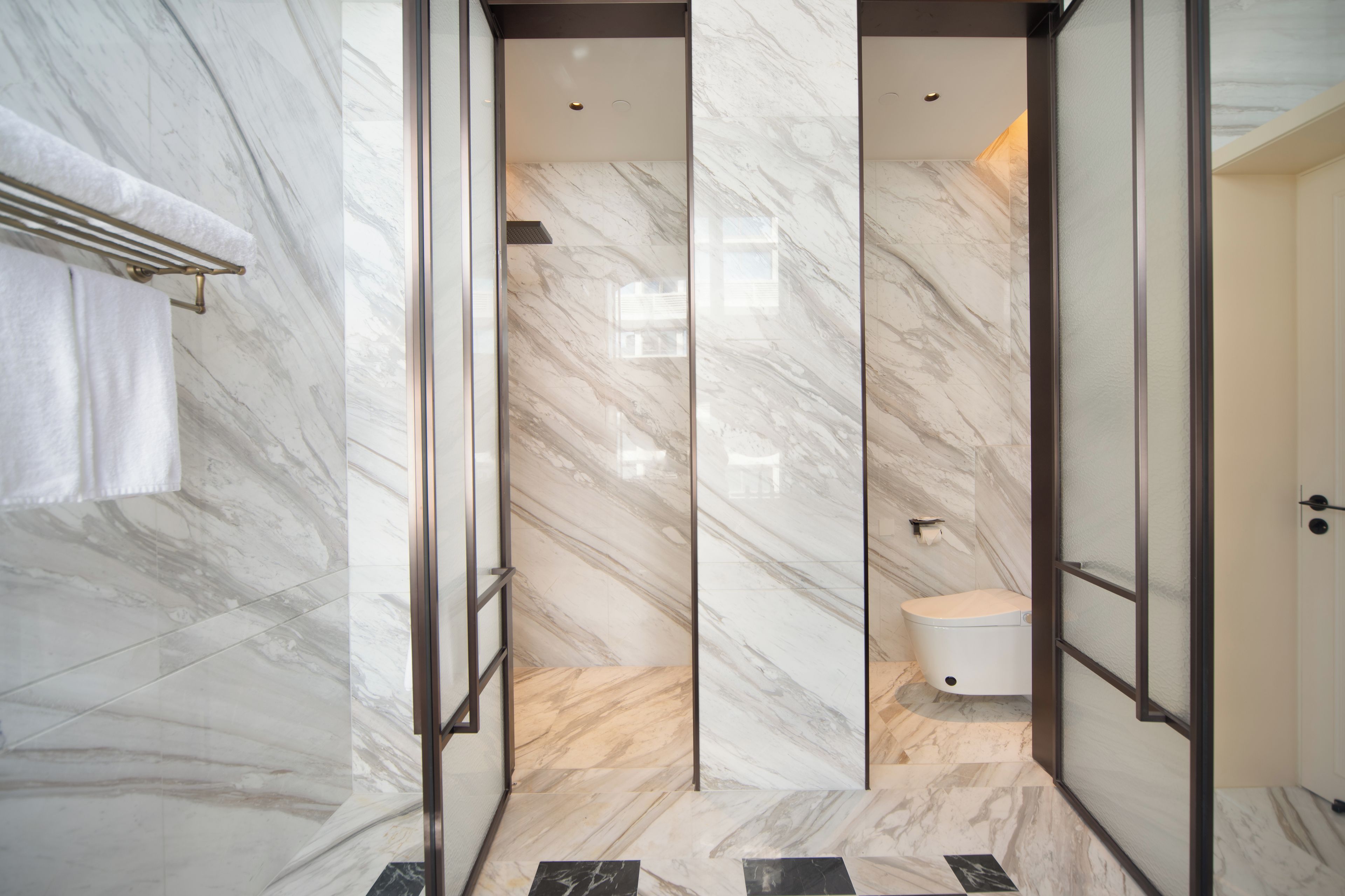 A modern bathroom with marble walls, a glass shower enclosure, and a toilet.