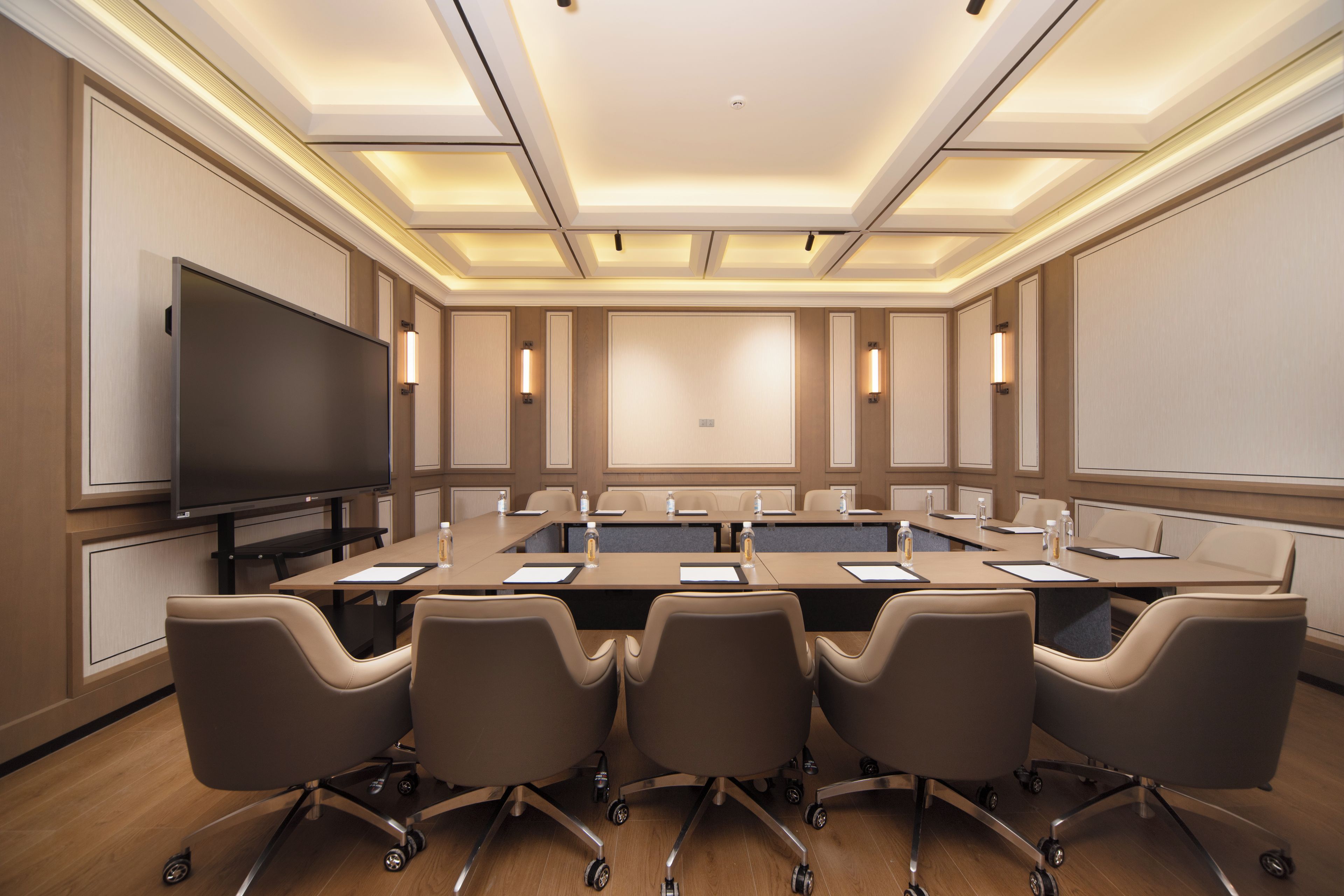 Un salón de conferencias con una gran pantalla plana, varias mesas y sillas.