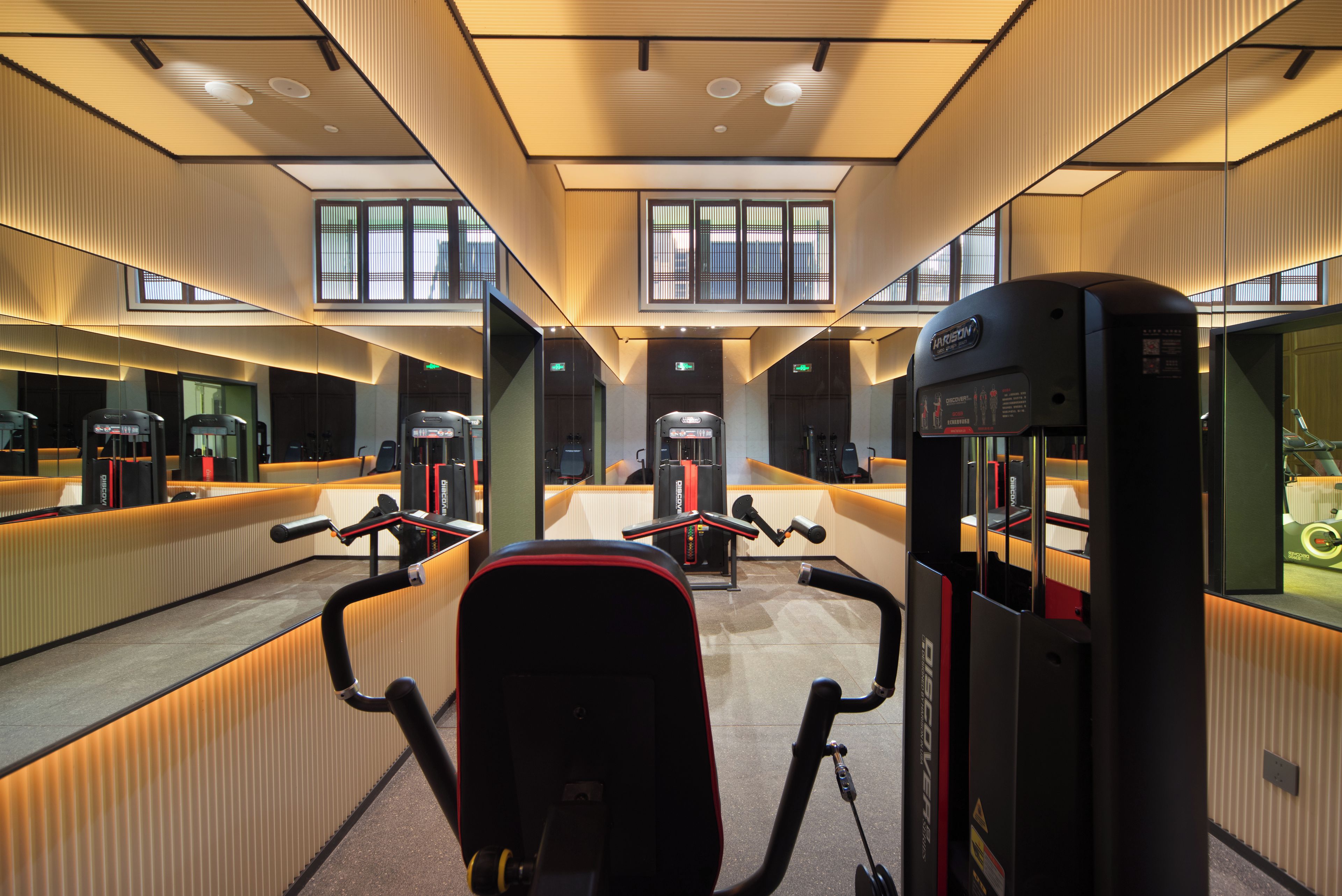 Une salle de sport équipée de matériel d’exercice, de miroirs et dotée d’un plafond haut avec des fenêtres.