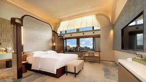 Una habitación de hotel moderna con una cama grande, una zona de estar y vistas a la ciudad.