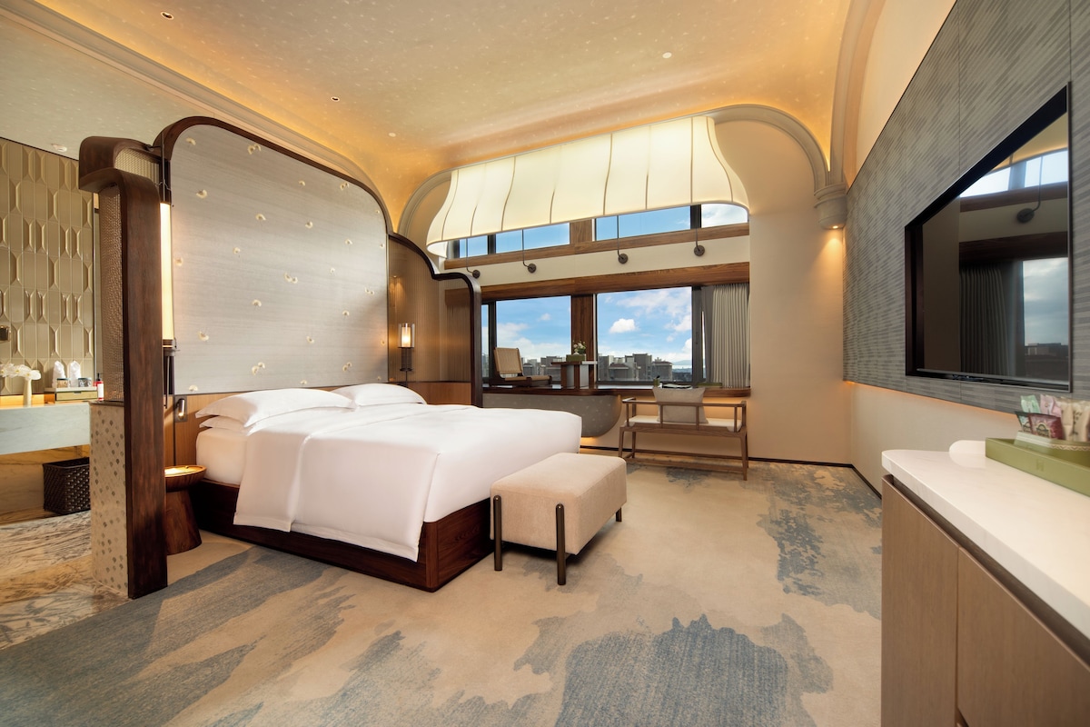 Una habitación de hotel moderna con una cama grande, una zona de estar y vistas a la ciudad.
