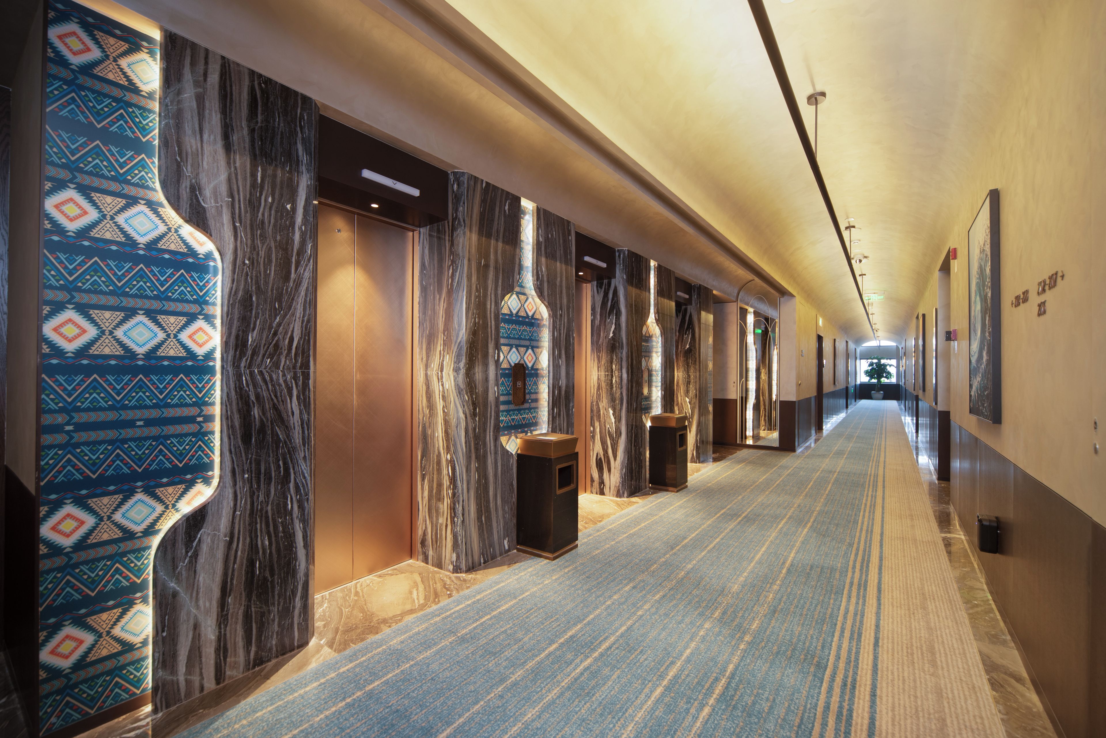 Un pasillo de hotel con paredes de mármol, papel tapiz estampado y suelo alfombrado.