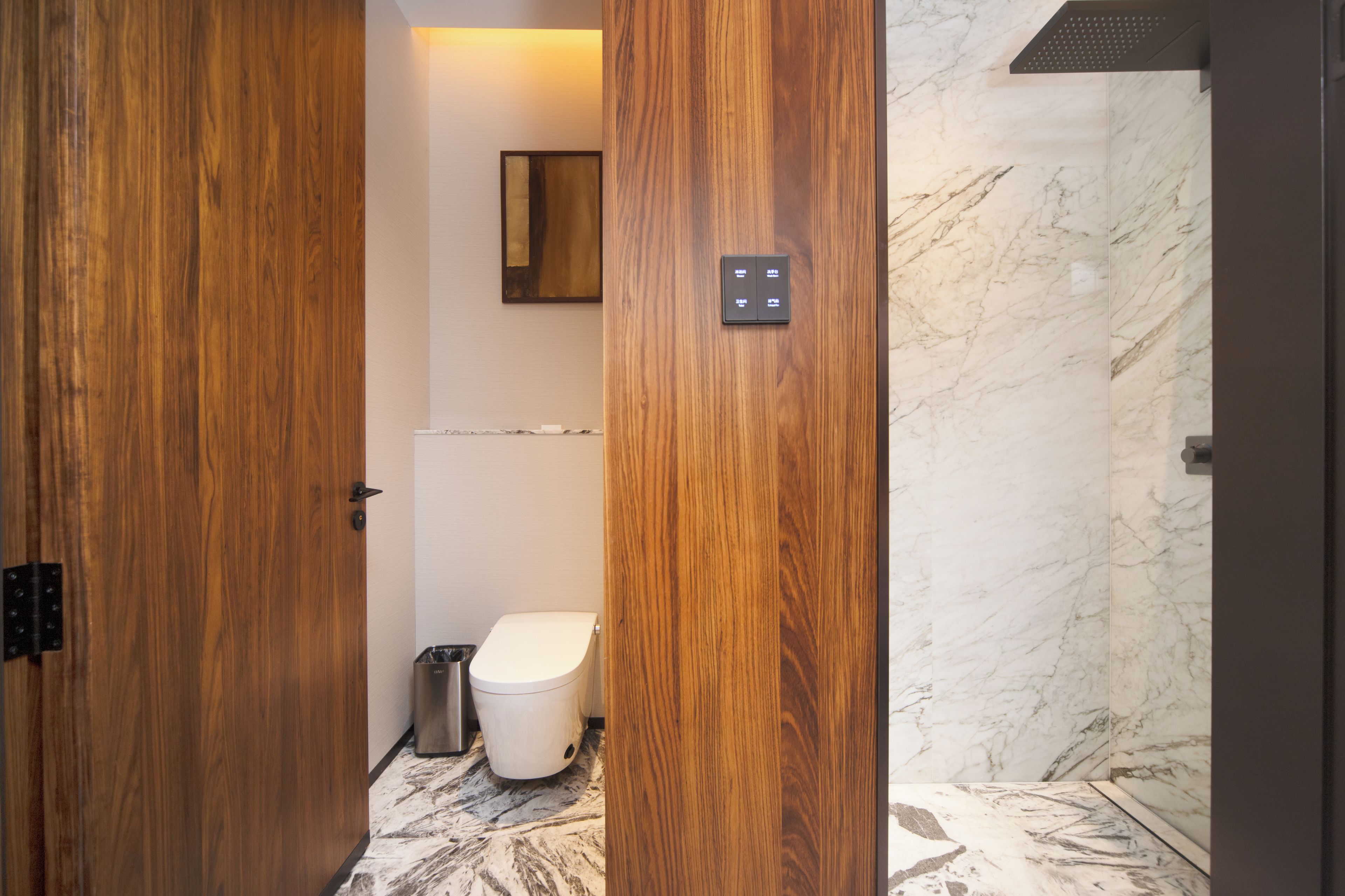 Un bagno moderno con porte in legno, rivestimento doccia in marmo e un water con cestino.