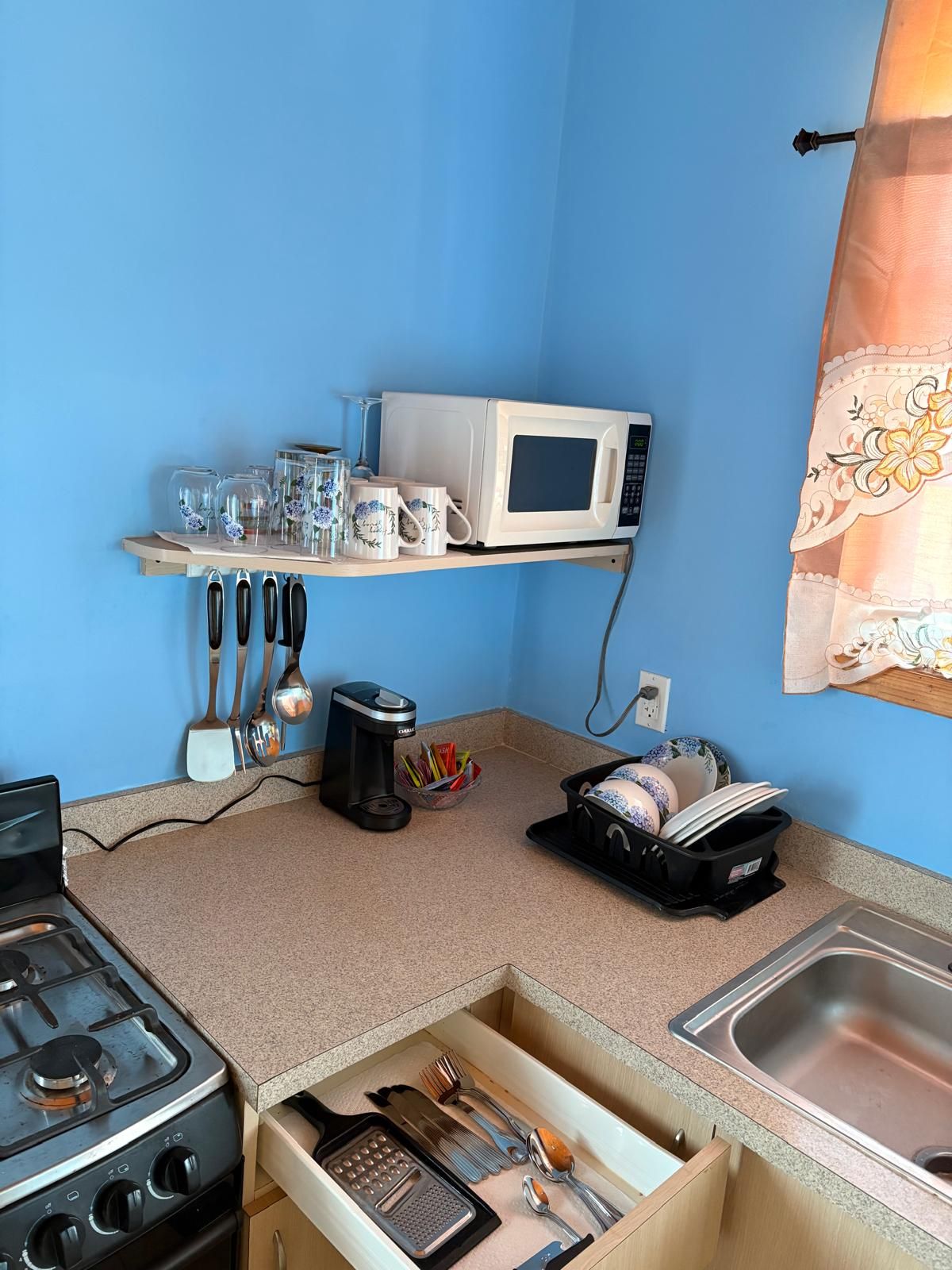 Een kleine keuken met een magnetron, koffiezetapparaat en een afwasschaal.