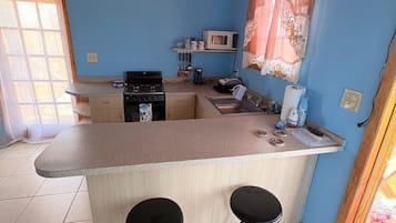 Une cuisine compacte dotée d’un îlot central, de deux tabourets, d’un four à micro-ondes et d’une cuisinière.
